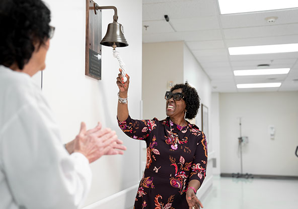 Debra rings a bell in a hospital, signifying she is in full remission after having aggressive breast cancer. 