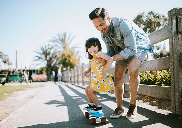 A dad teaches his young daughter how to skateboard